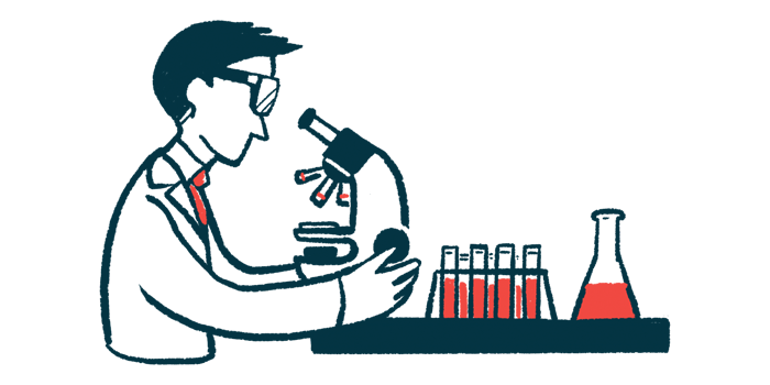 A scientist looks through a microscope in a lab, with test tubes and a flask on the counter nearby.
