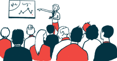 A person points to a screen on a wall while making a presentation to a crowd.